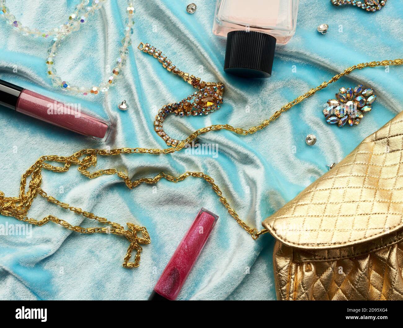golden handbag, lip gloss and beads on a blue background, top view. Stock Photo