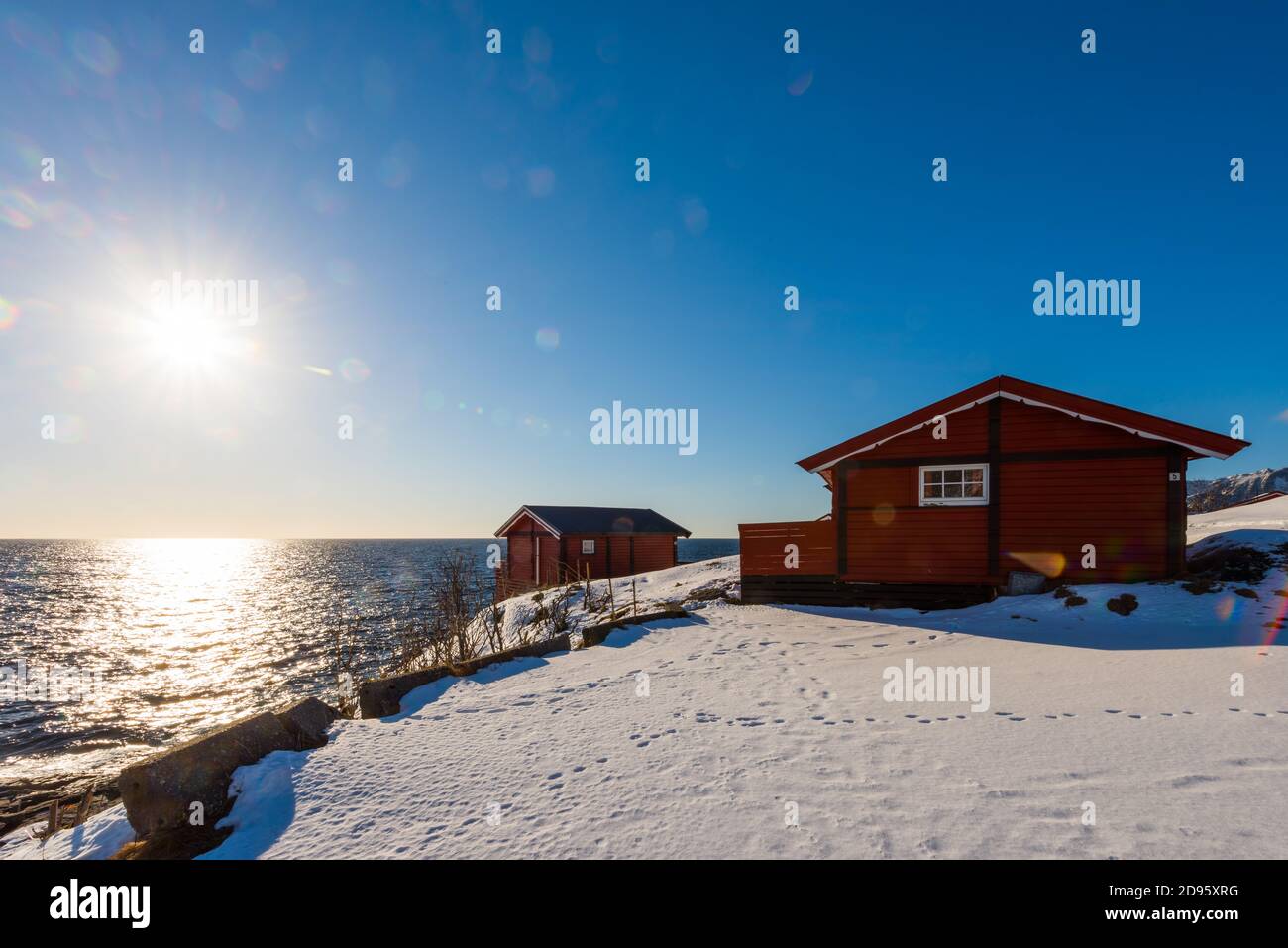 Sun flare on renovated traditional red rorbu fishing hut with empty racks for drying cod on the Lofoten islands in Norway in winter on the coast Stock Photo