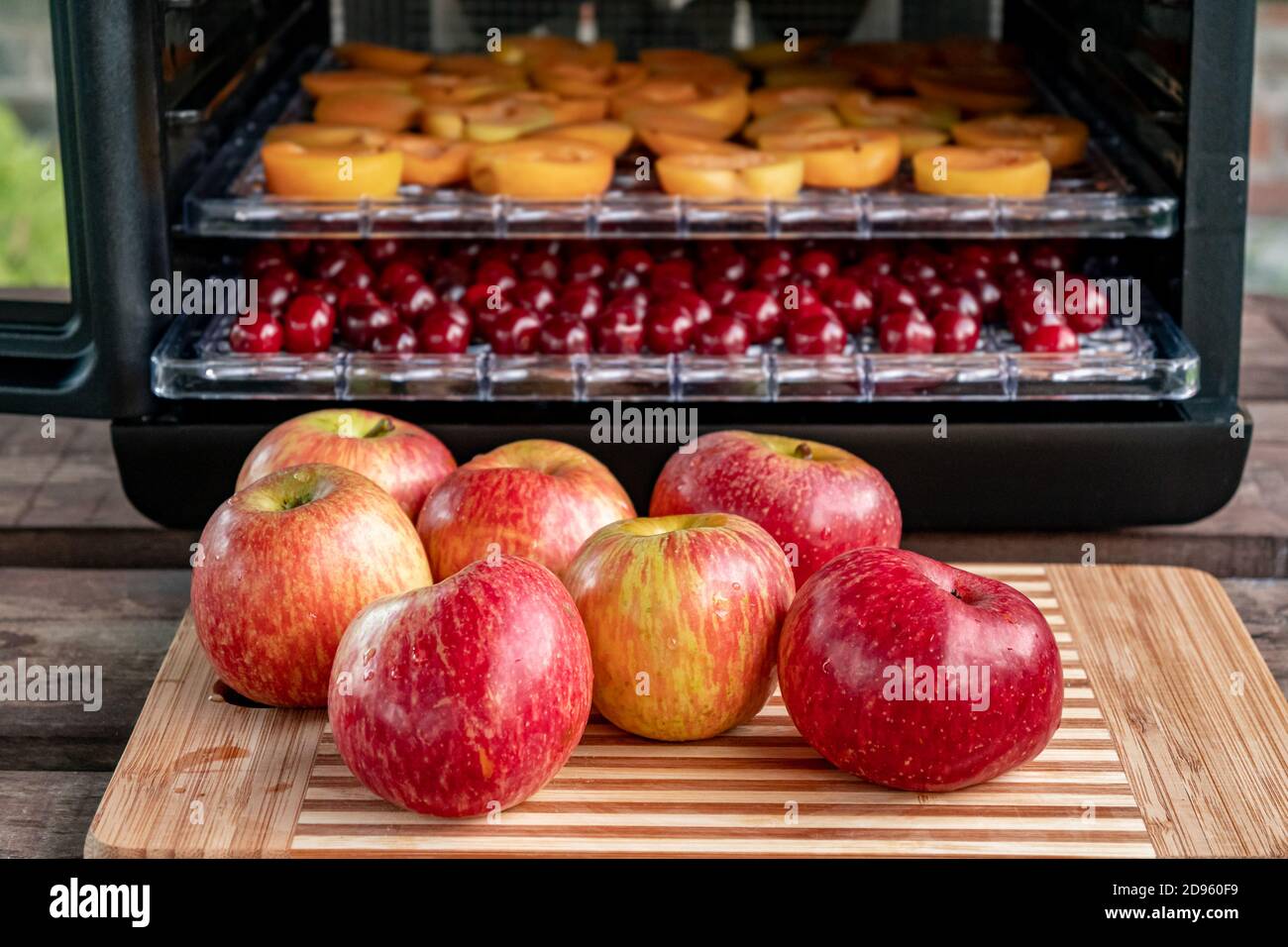 Fresh red apples on a chopping Board. In the background, a drying machine for dehydrating products with horizontal loading of pallets. There are apric Stock Photo