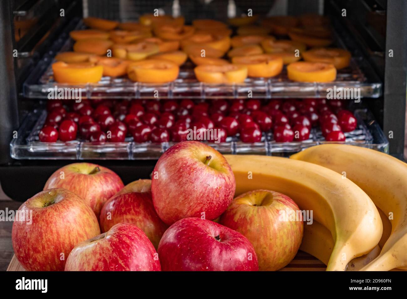 Fresh red apples and bananas on a chopping Board. In the background, a drying machine for dehydration with horizontal loading of trays. There are apri Stock Photo