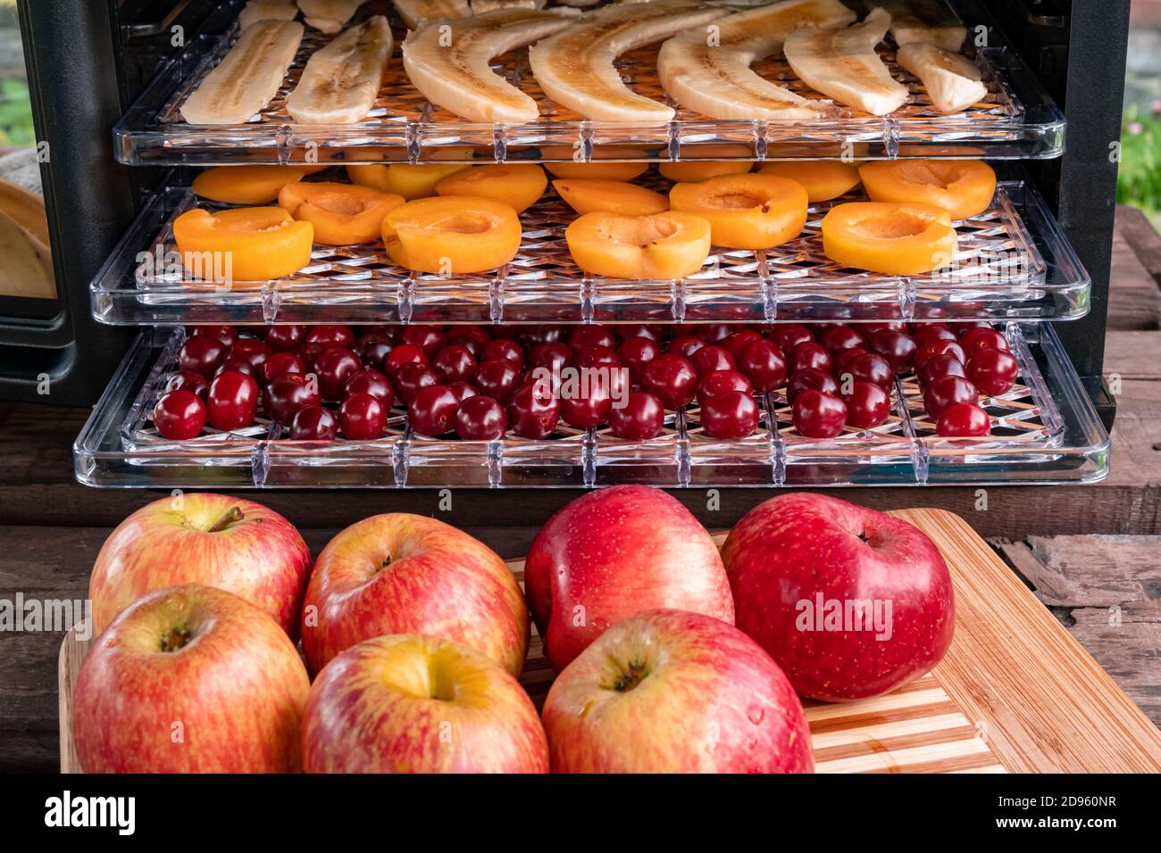 Fresh red apples on a chopping Board. In the background, a drying machine for dehydration with horizontal loading of pallets. There are bananas, apric Stock Photo