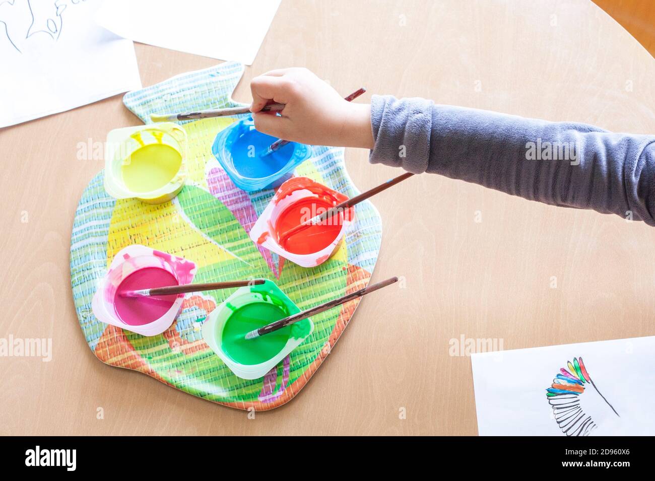 Child hand soaking artist brush on Washable Tempera paint. Yogurt cups