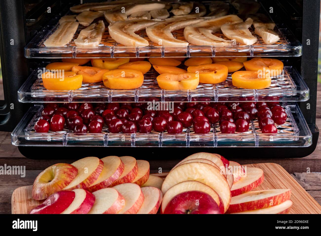 Sliced red apples on a chopping Board. In the background, a drying machine for dehydration with horizontal loading of pallets. There are bananas, apri Stock Photo