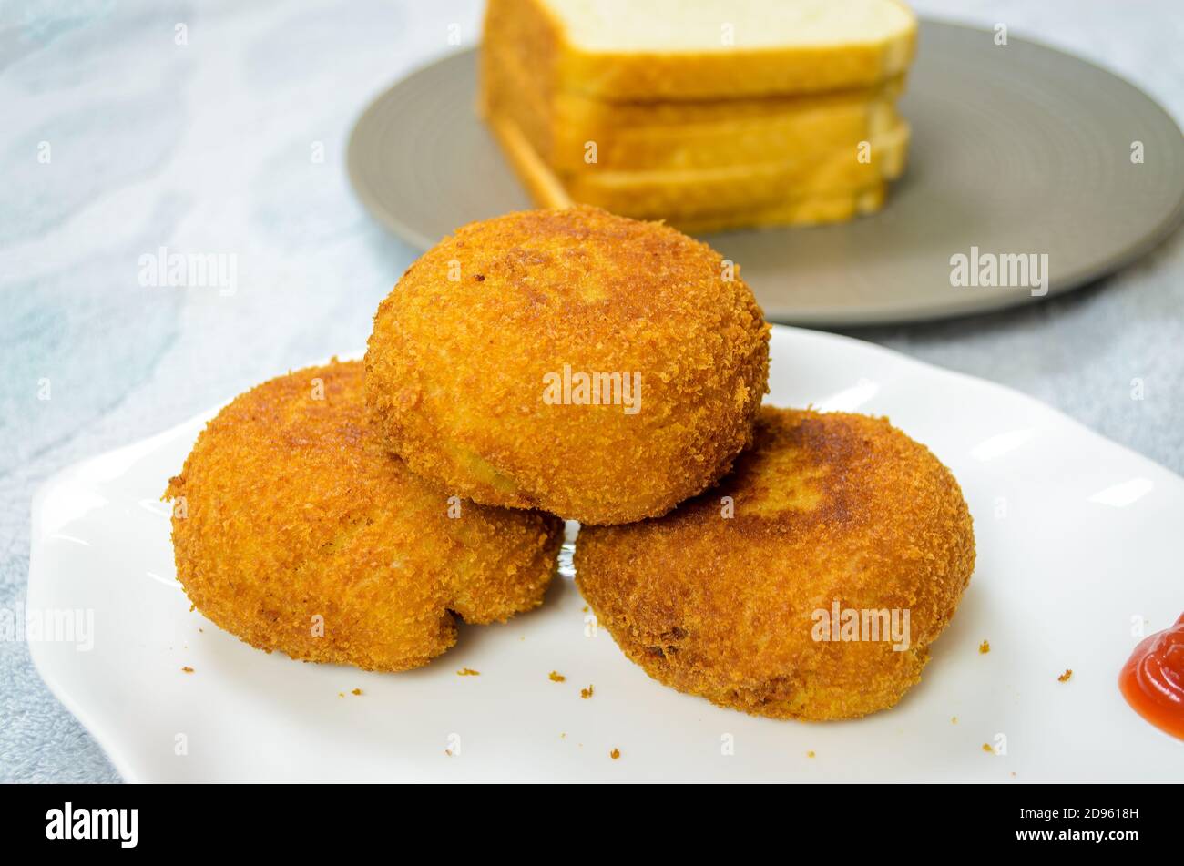 Three Chicken Bread Cutlets on top of each other with Bread slices in the background Stock Photo