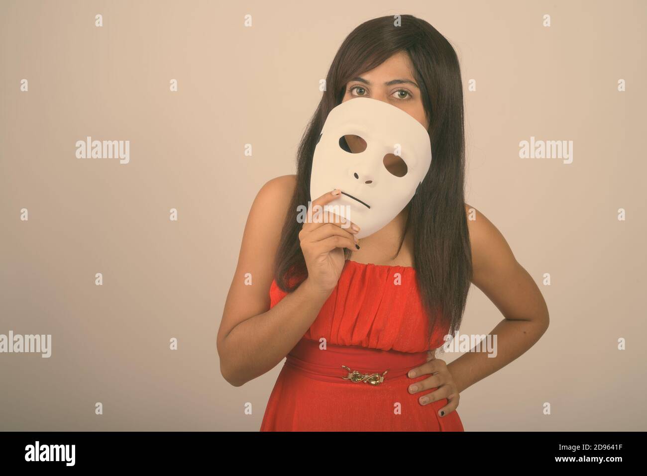 Studio shot of young Persian woman covering face with white mask against gray background Stock Photo