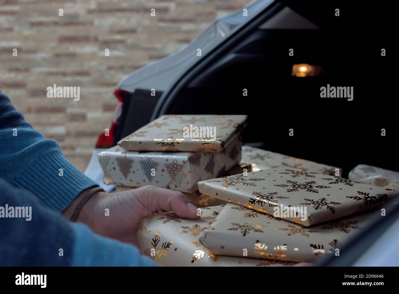 A man consumer takes out of the car Christmas gifts that he has just bought to put under the Christmas tree at home. Christmas photography 2020. Stock Photo