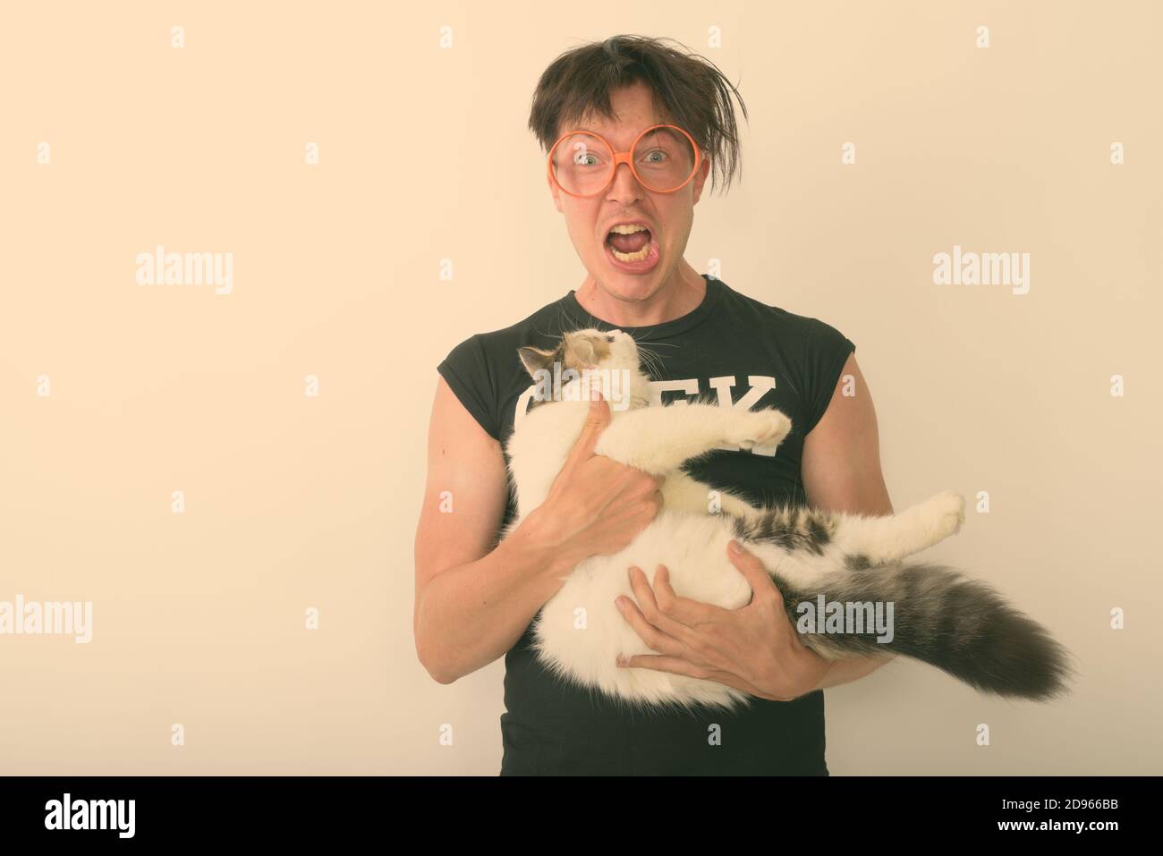 Studio shot of young nerd man looking excited while holding cute cat and wearing eyeglasses against white background Stock Photo