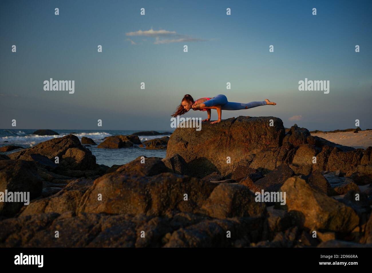 Young woman with long hair is practicing yoga pose bakasana on rocks