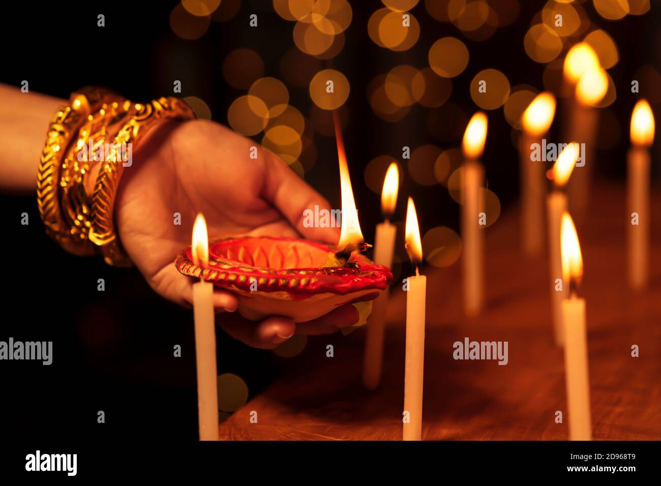 Indian housewife or bride woman wearing traditional gold jewelry, lighting candles with a clay diya or oil lamp in one hand at a temple on Diwali nigh Stock Photo