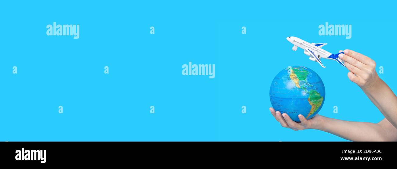 Travel concept. Female hands holding globe and figurine of passenger plane on blue background. The plane is flying to the globe. Wide format banner Stock Photo