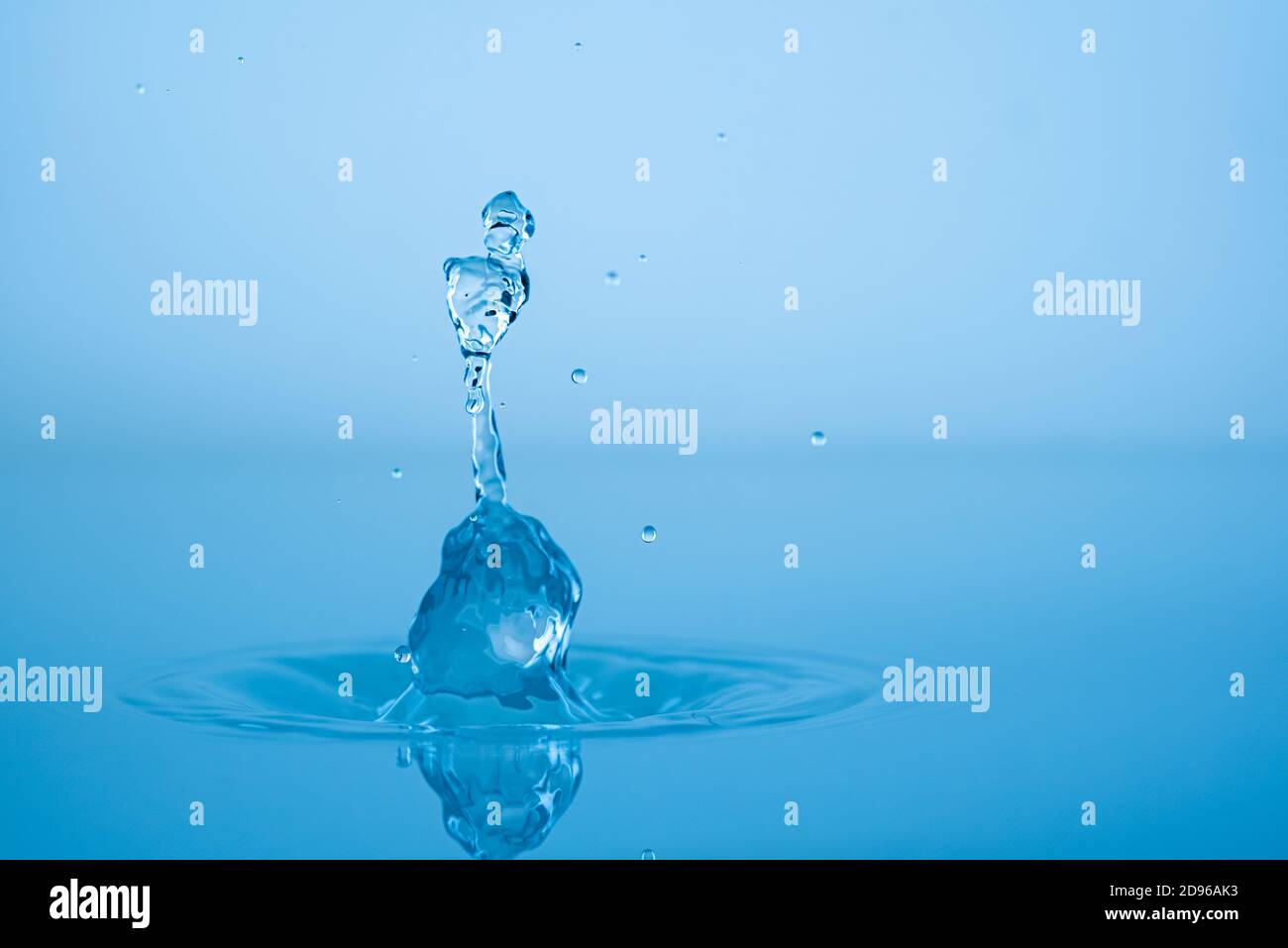 Water drop splashing into blue water surface Stock Photo - Alamy