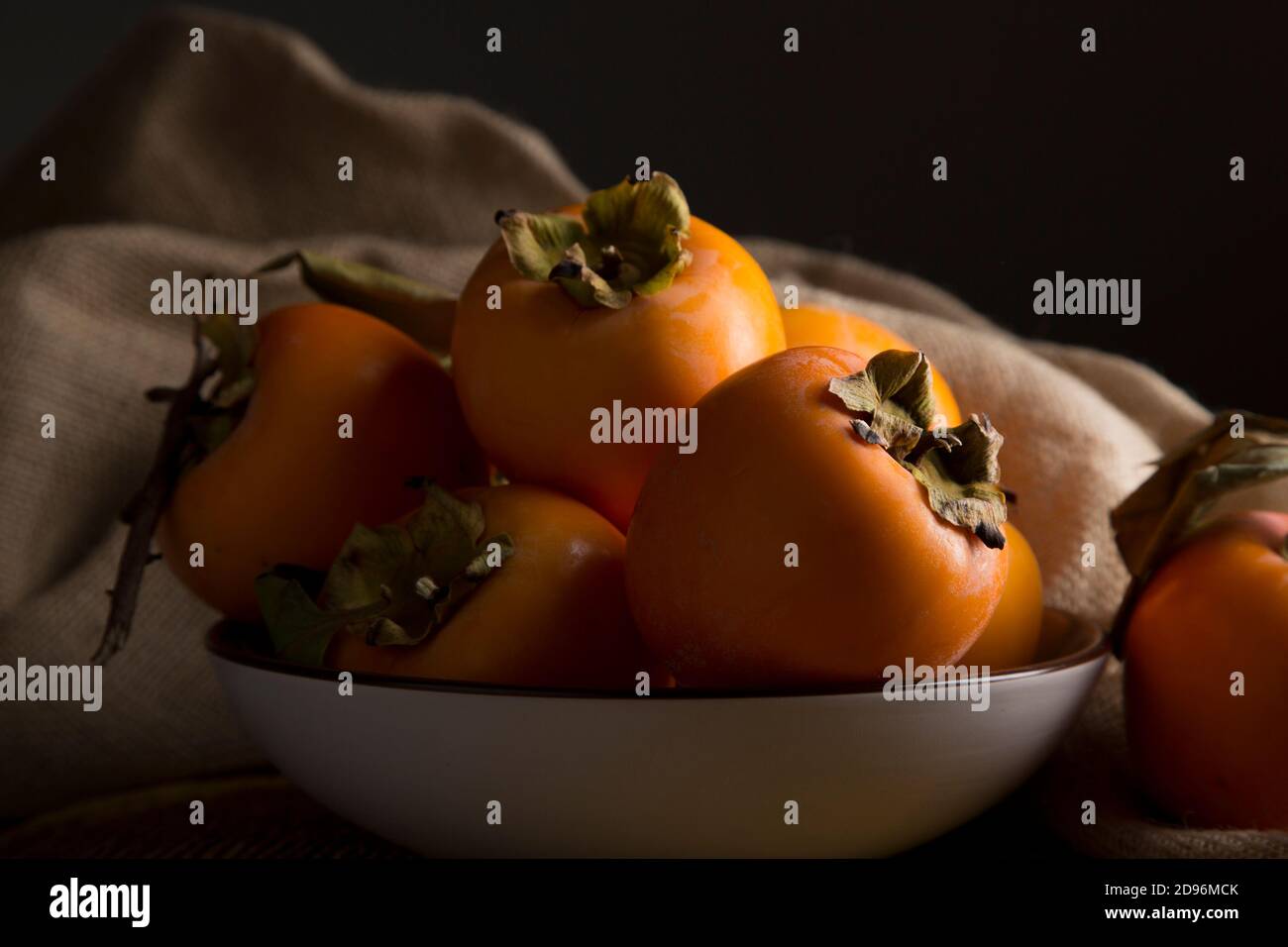 Still life with kakis and persimmon on brown wooden table in low key Stock Photo