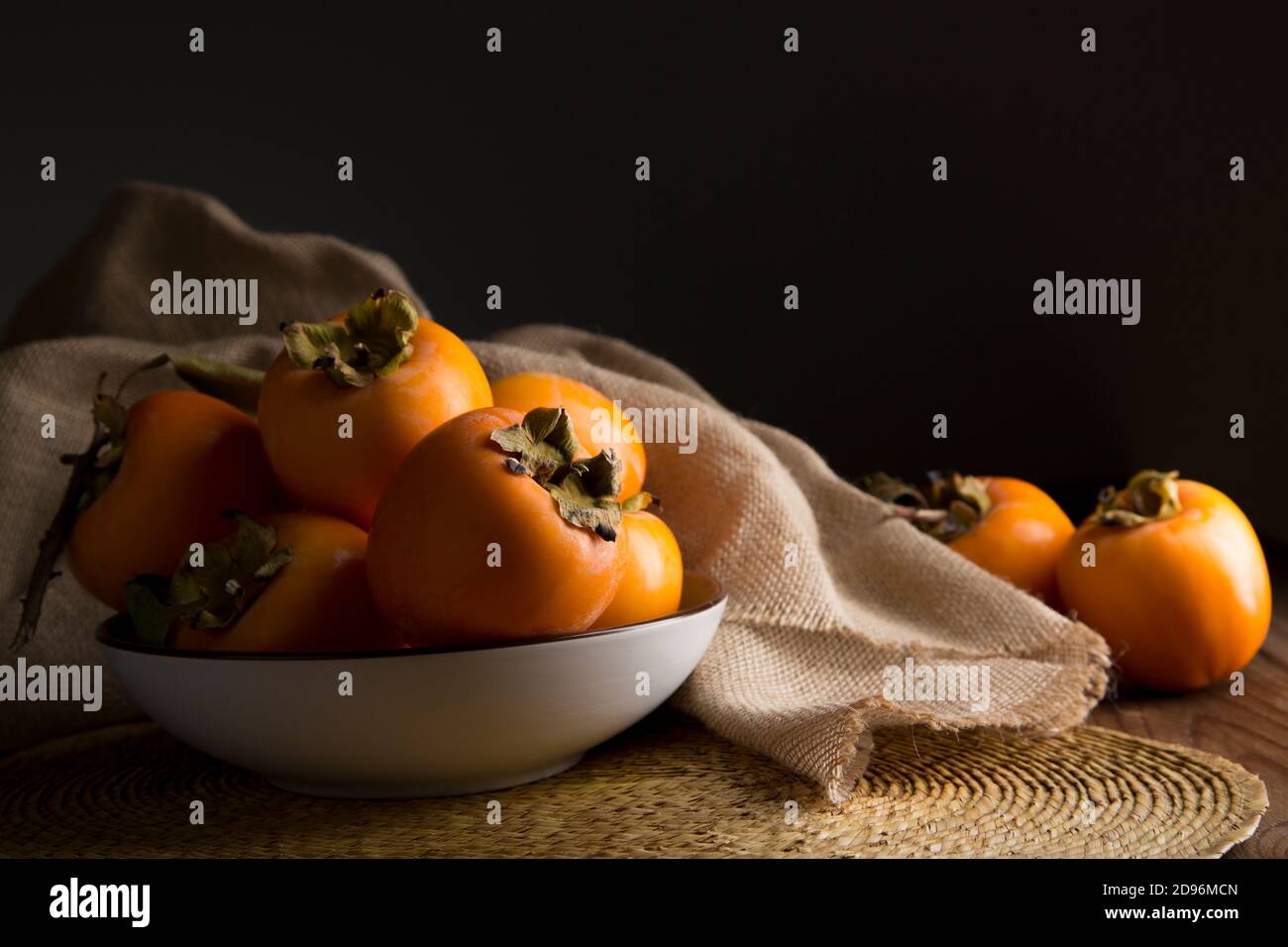Still life with kakis and persimmon on brown wooden table in low key Stock Photo