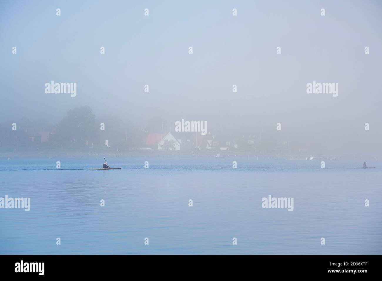 Stay fit rowing a canoe or kayak amidst the mist on a gloomy day. People keep fit kayaking amid tranquility on a still, calm Baltic sea by the coast Stock Photo