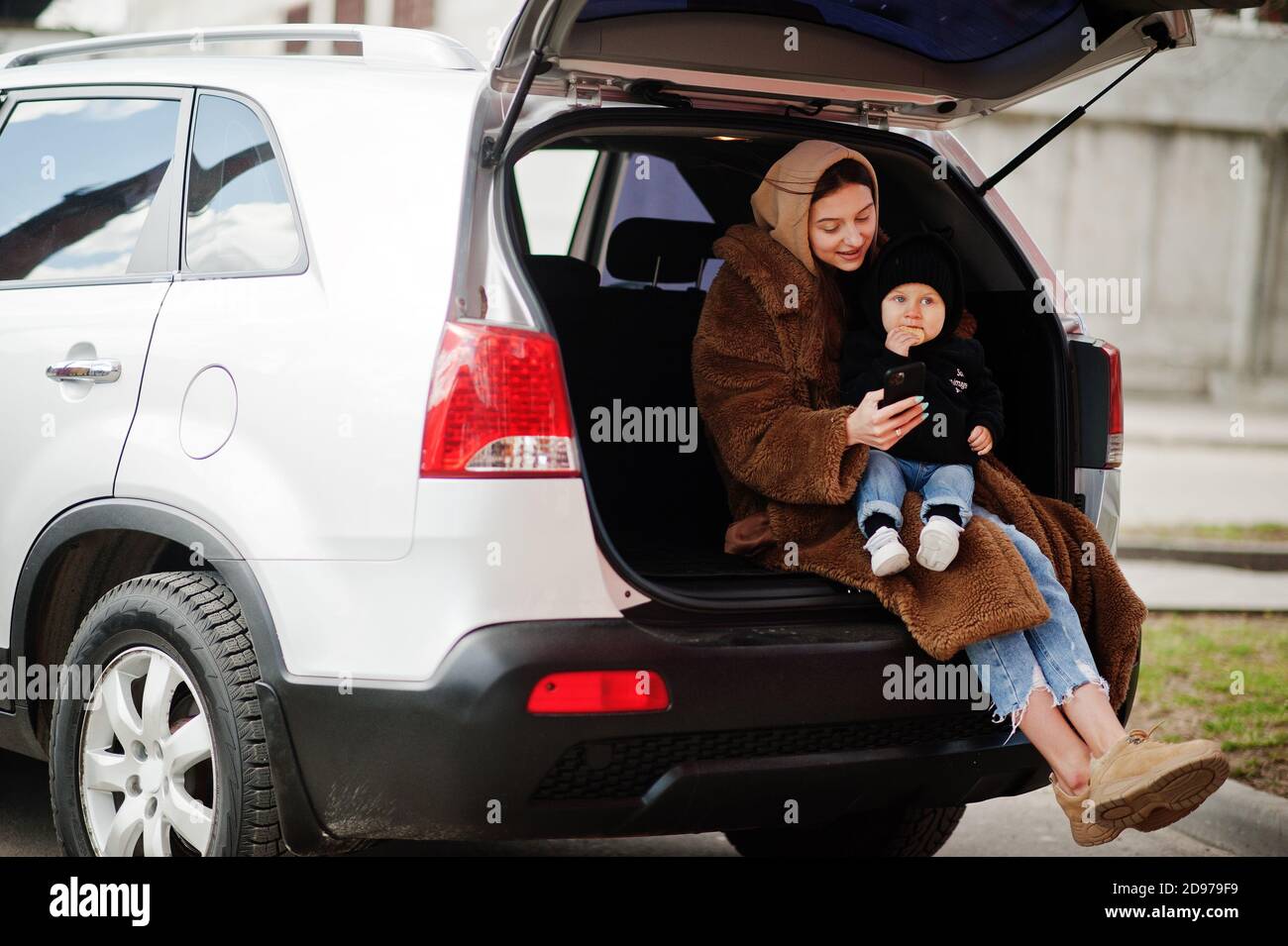 Young mother and child sitting in the trunk of a car and looking at ...