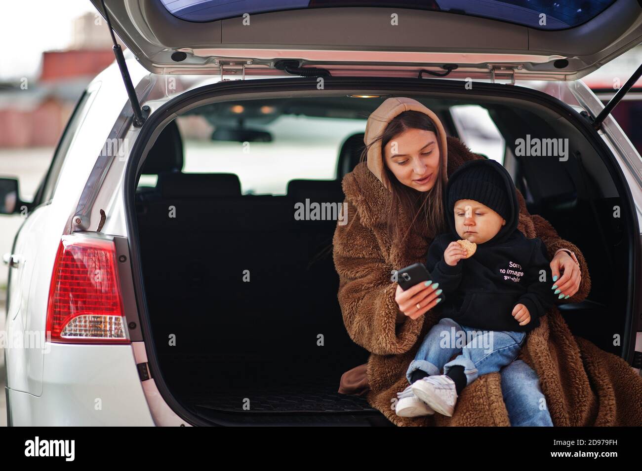 Young mother and child sitting in the trunk of a car and looking at