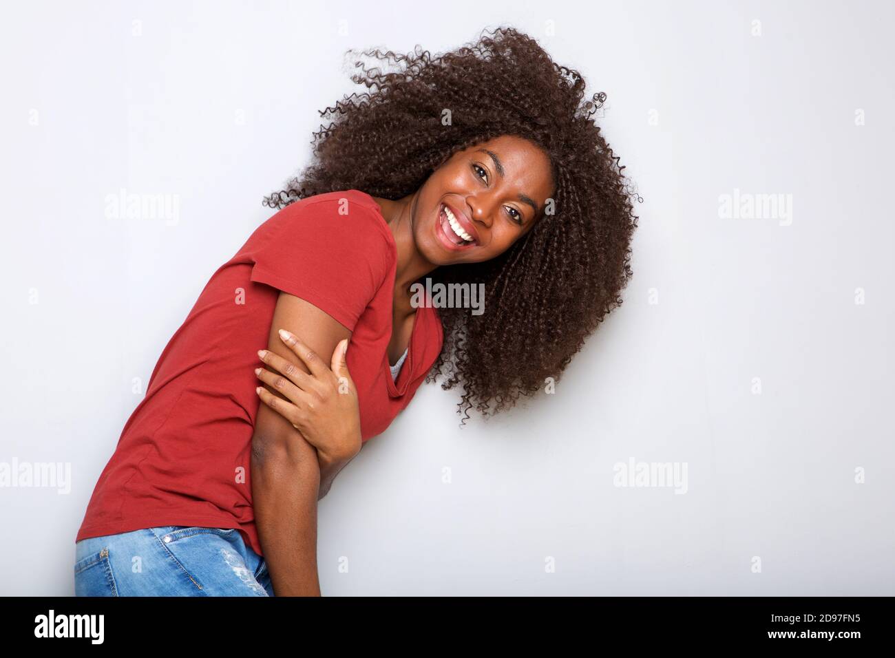 Portrait of beautiful young black woman laughing against white wall ...