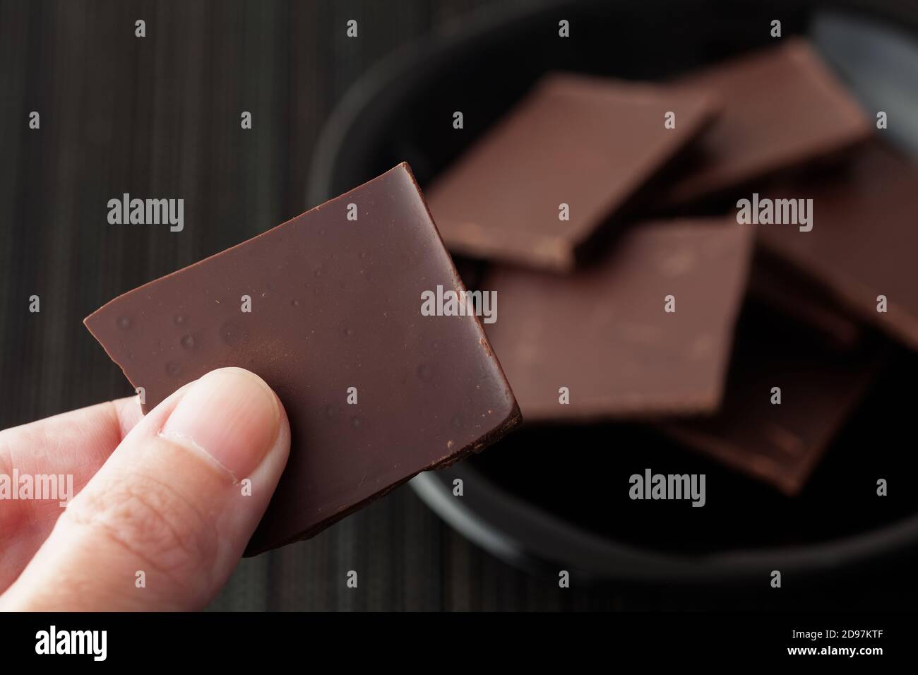 Man holding a piece of broken dark chocolate. Low key. Stock Photo