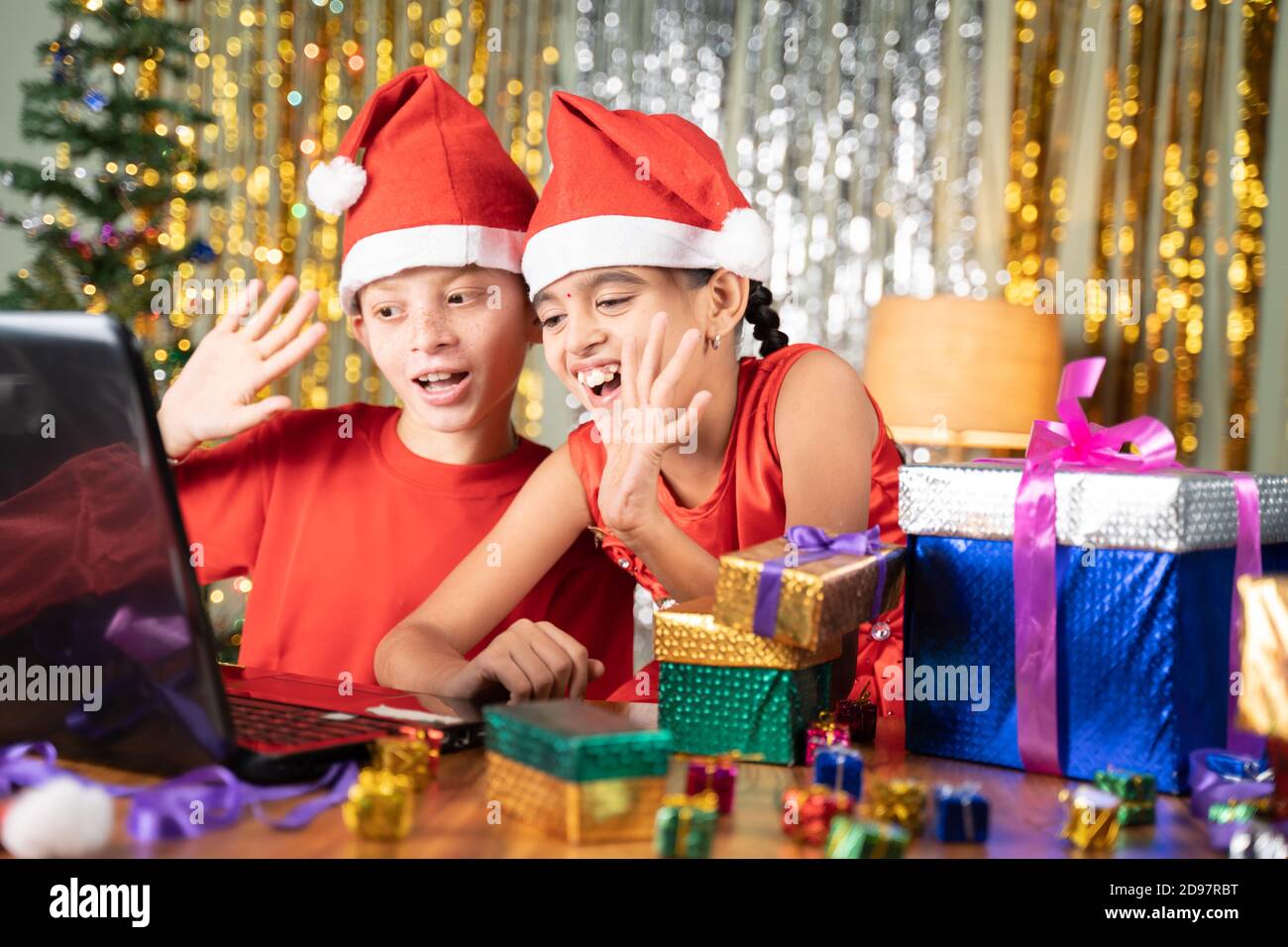 Kids got the xmas gift and Opening gift infront of Laptop on video call at home with decorated background during christmas celebration Stock Photo
