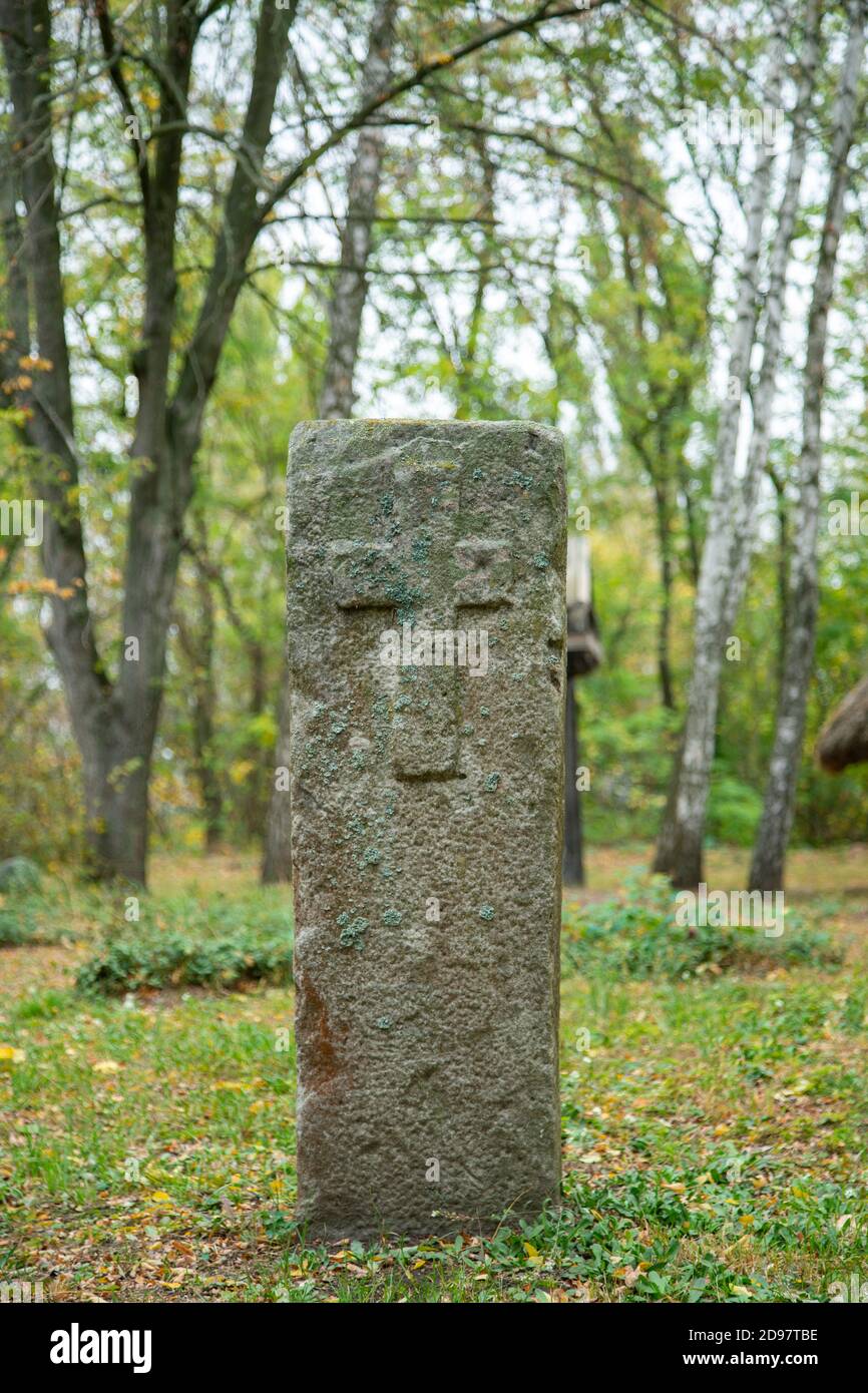 A worn sandstone grave marker in the shade on a very bright day. There is no text visible on the stone, but there is some moss on the top. Tombstone Stock Photo