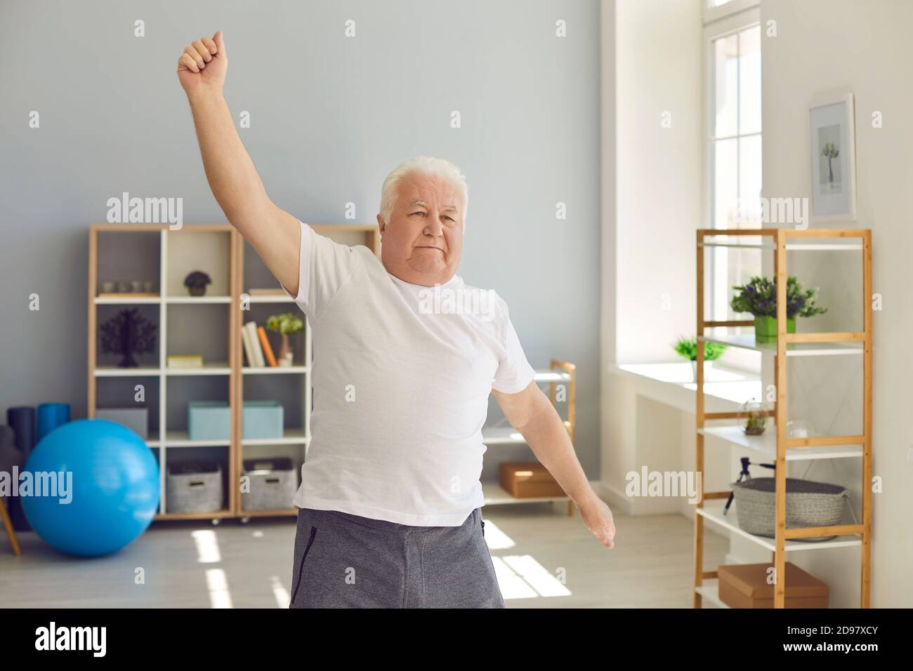 Smiling positive elderly man doing exercises or light fitness training at home or in rehabilitation center Stock Photo
