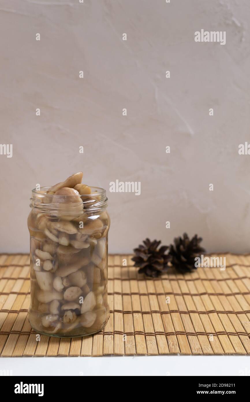 Pickled forest mushrooms in a glass jar with pine cones on a wooden background. Autumn gifts. Vertical orientation. Copy space. Stock Photo