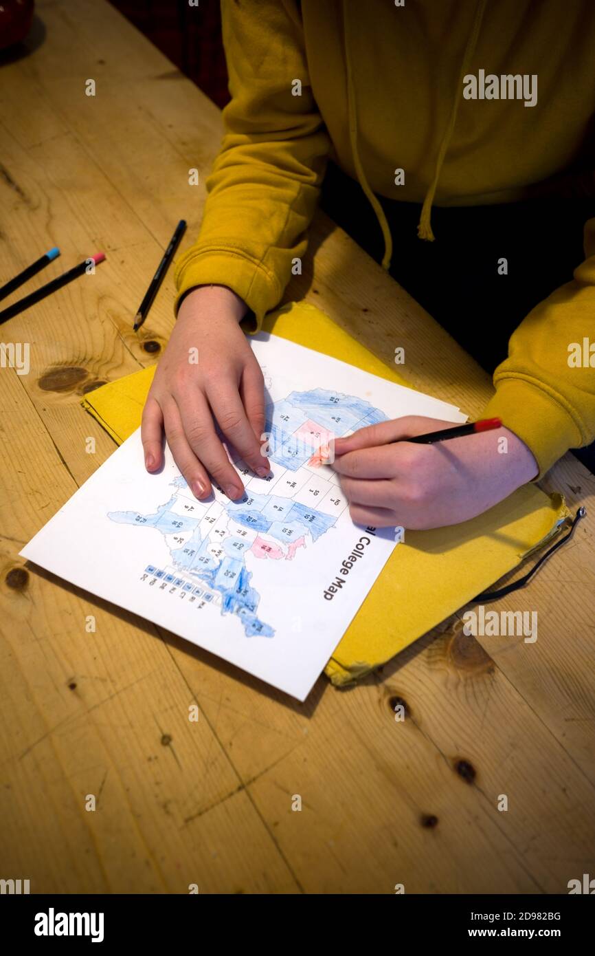 cropped view of young boy colouring in a print out of the 2020 electoral college vote map on a wooden kitchen table at home Stock Photo