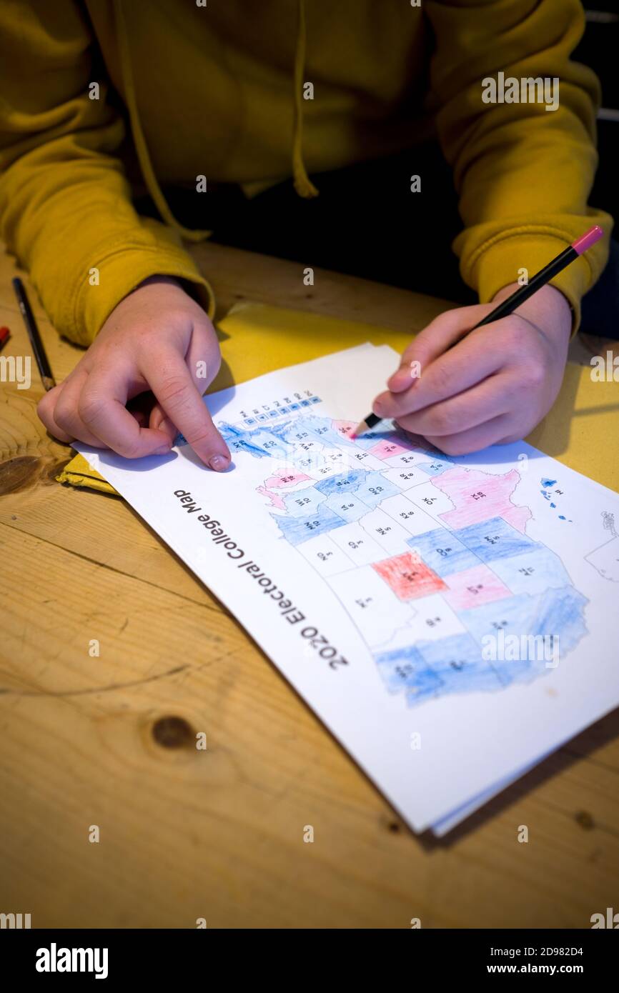 cropped view of young boy colouring in a print out of the 2020 electoral college vote map on a wooden kitchen table at home Stock Photo