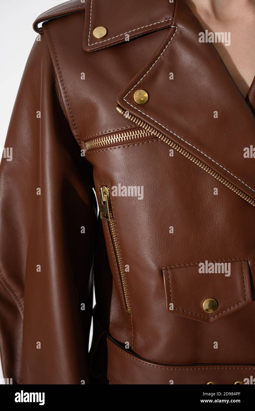 Brown leather jacket with metal zippers on it. Person in a stylish white jacket. Stitched leather. Closeup. Vertical fashion background. Stock Photo