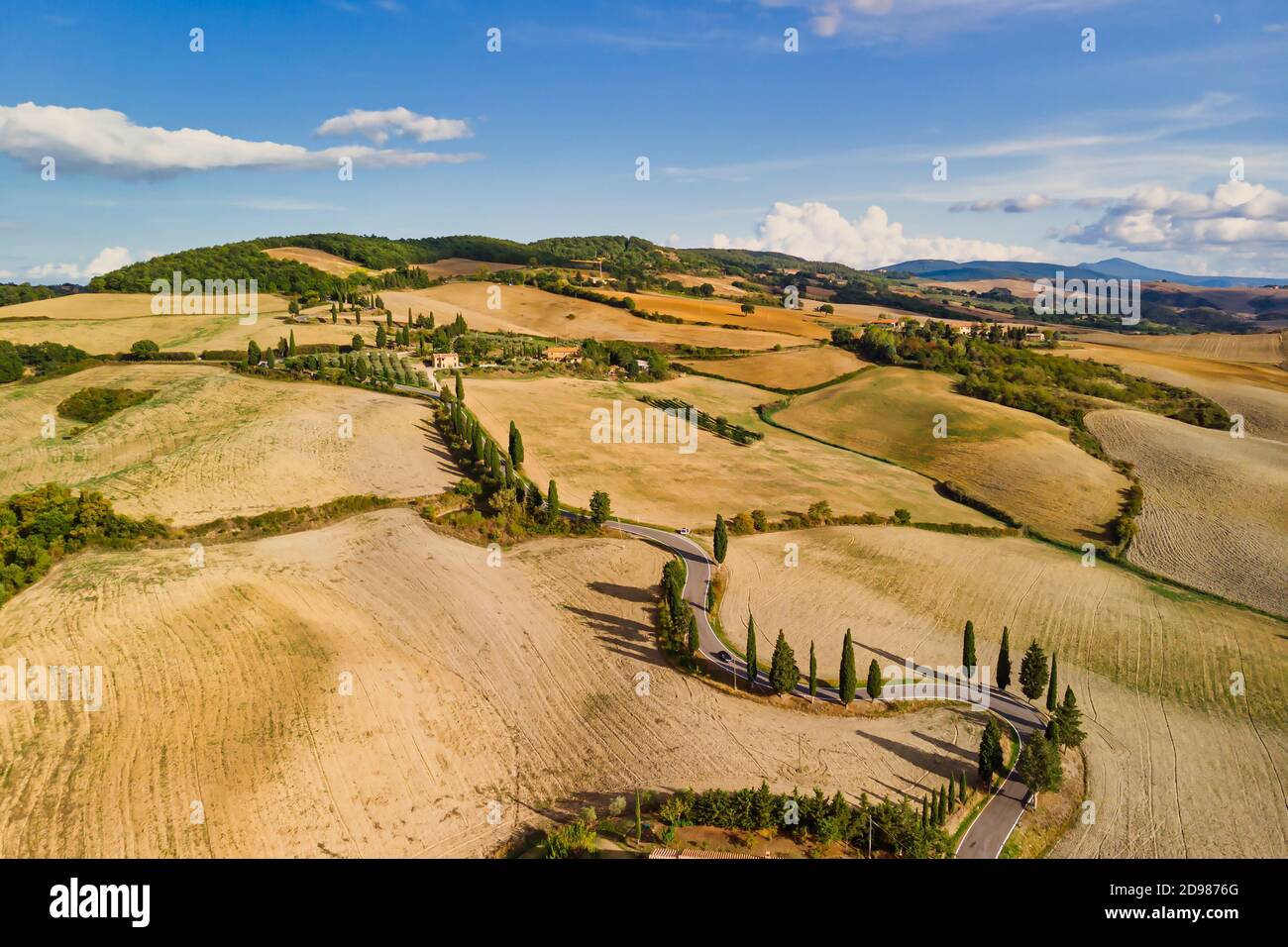 Summer landscape with winding road and golden crop fields near Pienza Tuscany Italy. Wide shot. Stock Photo