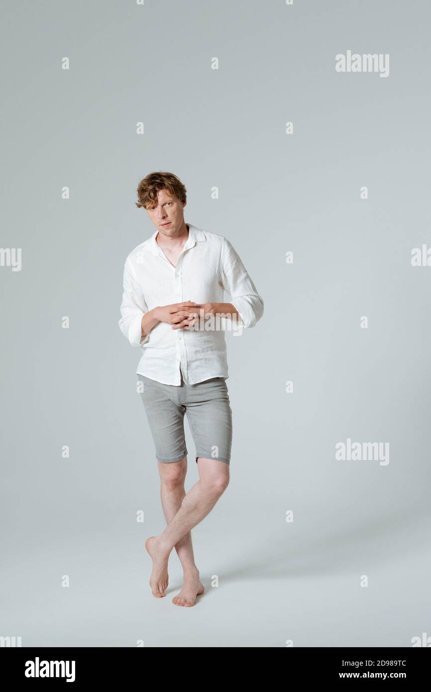 Pensive man standing full length folded arms and crossed legs. Thinking barefoot male model in white shirt demonstrates his emotions while posing on Stock Photo
