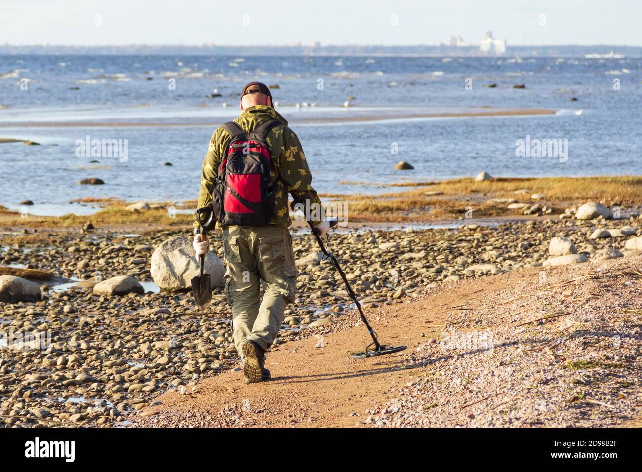 A treasure hunter with a metal detector walks along the sandy deserted beach in search of lost coins and jewelry. Stock Photo