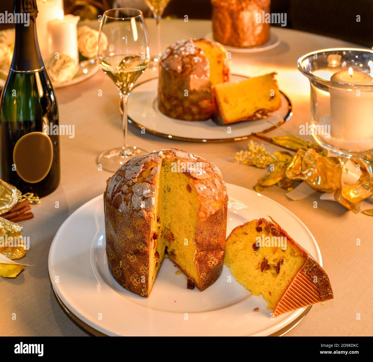 Panettone slice on table set in Christmas style, in the background bottle and glass of champagne and candles Stock Photo