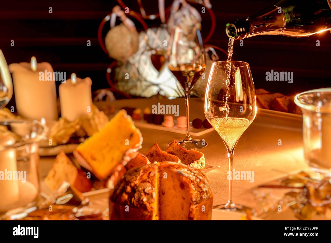 champagne is poured into glass on table set in Christmas style with blurred panettone and candles, warm mood light Stock Photo