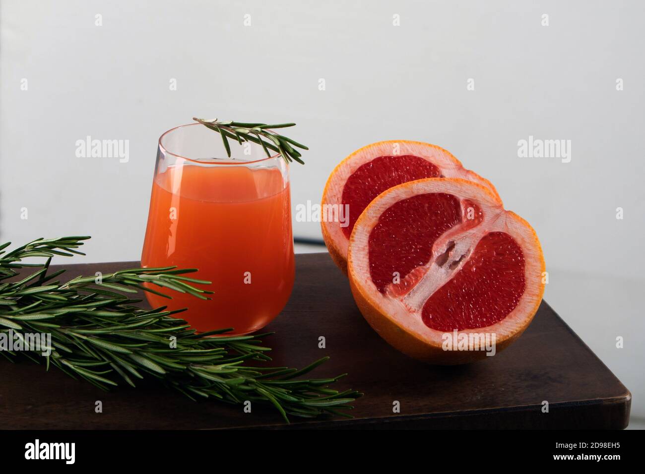 Two halves of red orange, rosemary sprig and glass of orange juice lying on a wooden table against light background Stock Photo