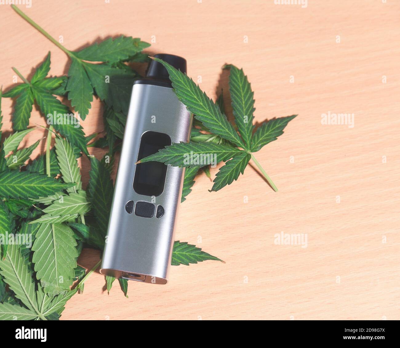 portable electronic vaporizer for smoking dry herbs next to hemp leaves on the table Stock Photo