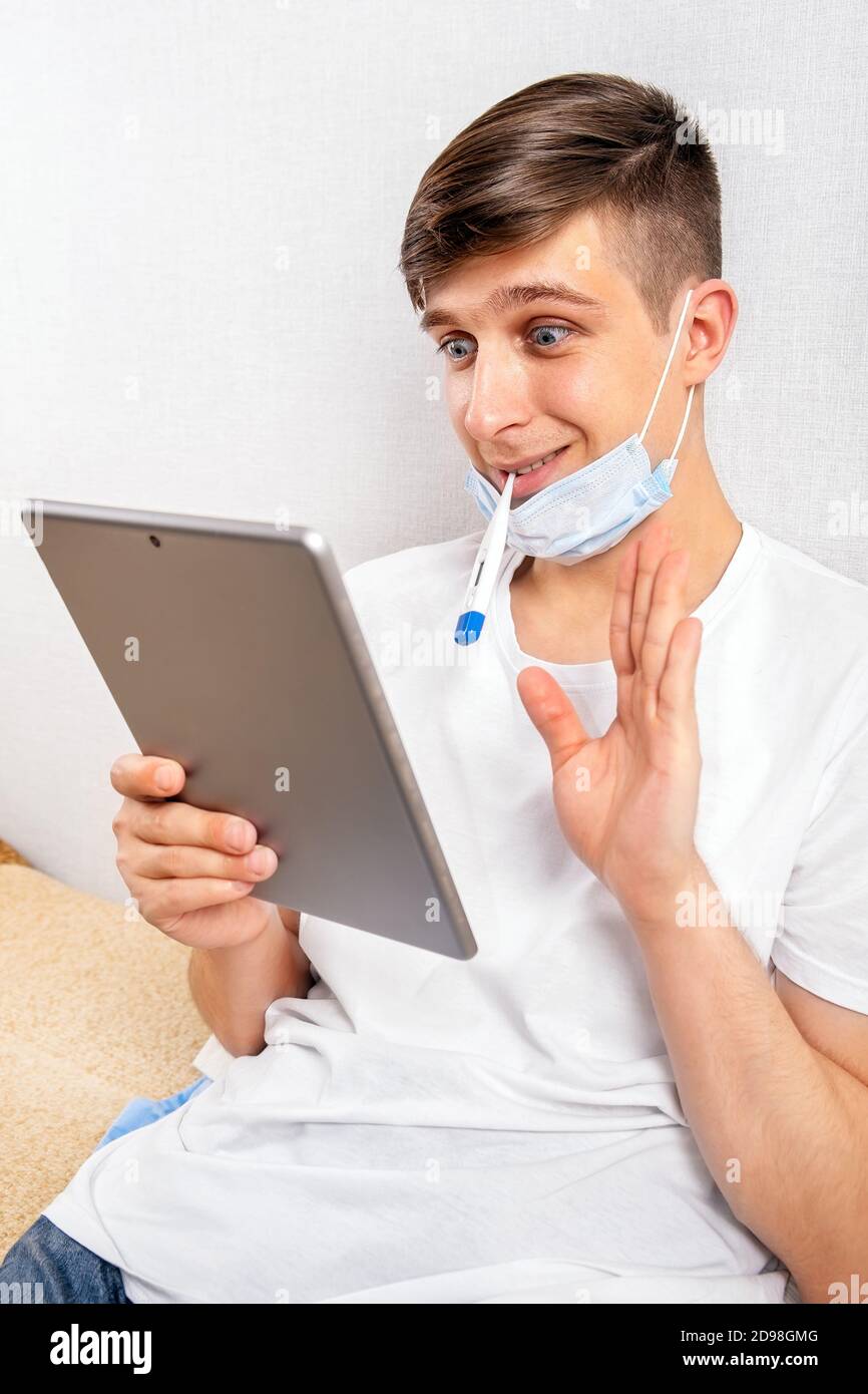 Cheerful Young Man with a Thermometer hold a Tablet by the Wall in the Room Stock Photo