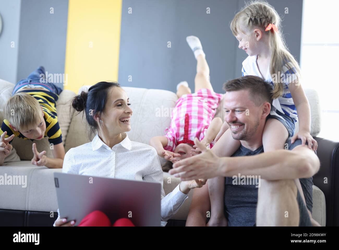 Family mom dad and children are sitting next to sofa with laptop laughing and indulging. Stock Photo