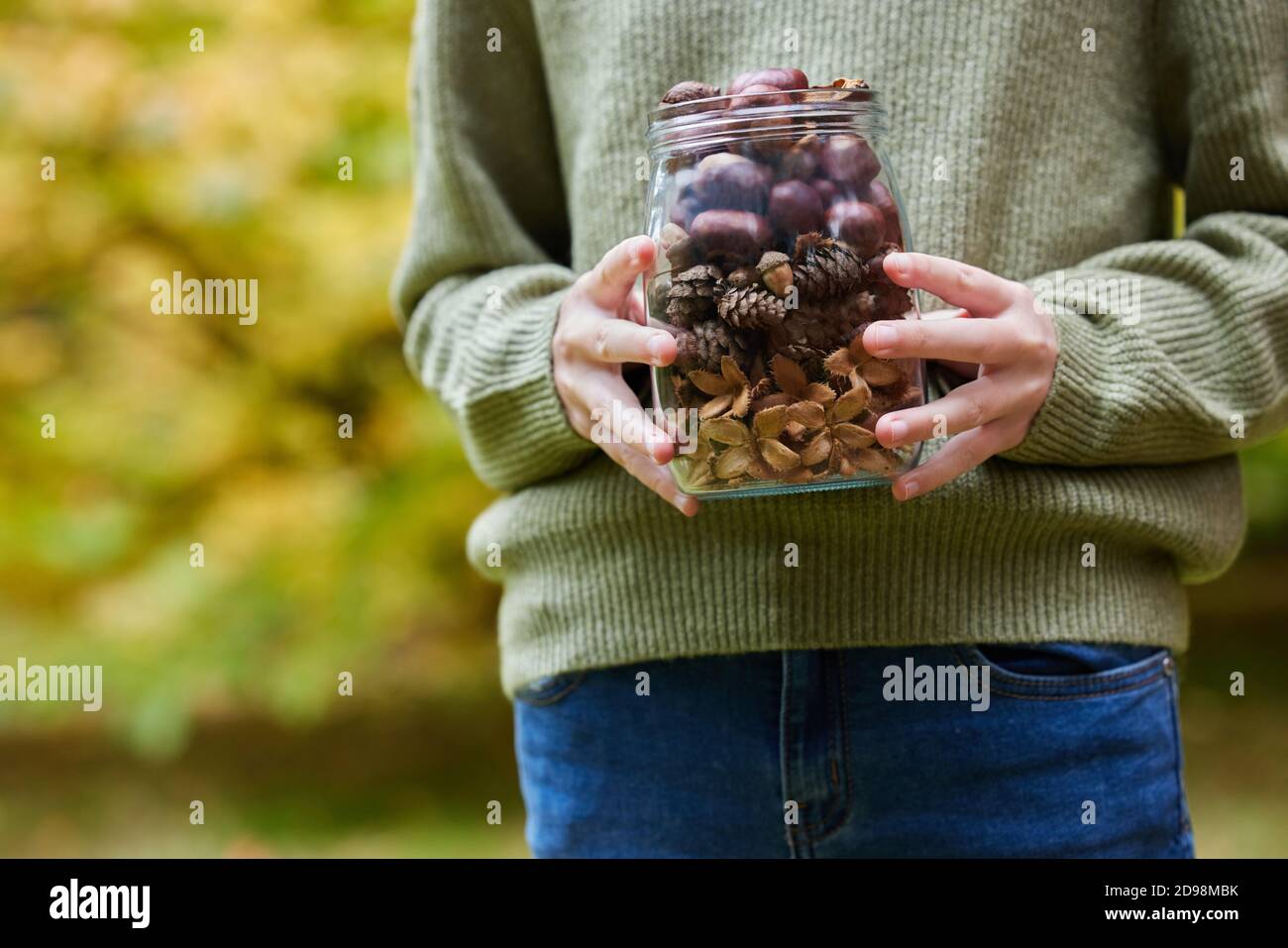 Close Up Of Girl Outdoors Holding Jar Of Autumn Pine Cones With Conkers Acorns And Beech Nut Cases Stock Photo