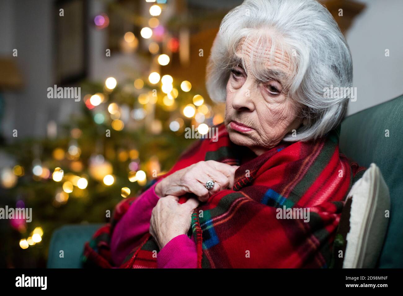 Sad And Lonely Senior Woman Unhappy About Spending Christmas At Home Alone Wrapped In Blanket Stock Photo