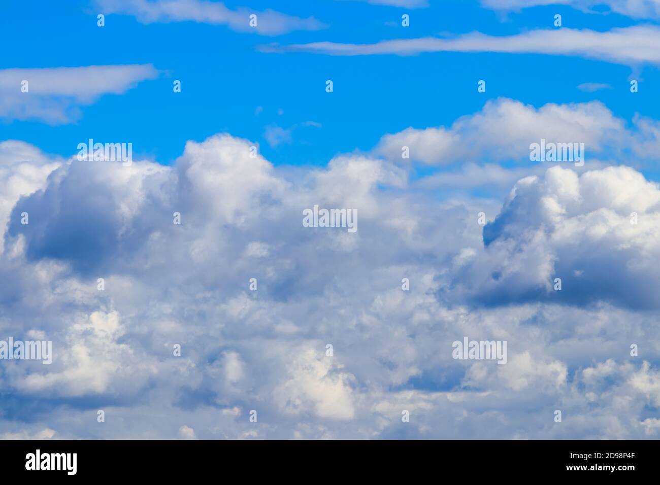 Bright blue sky with dramatic cumulus clouds lit by the daytime sun ...