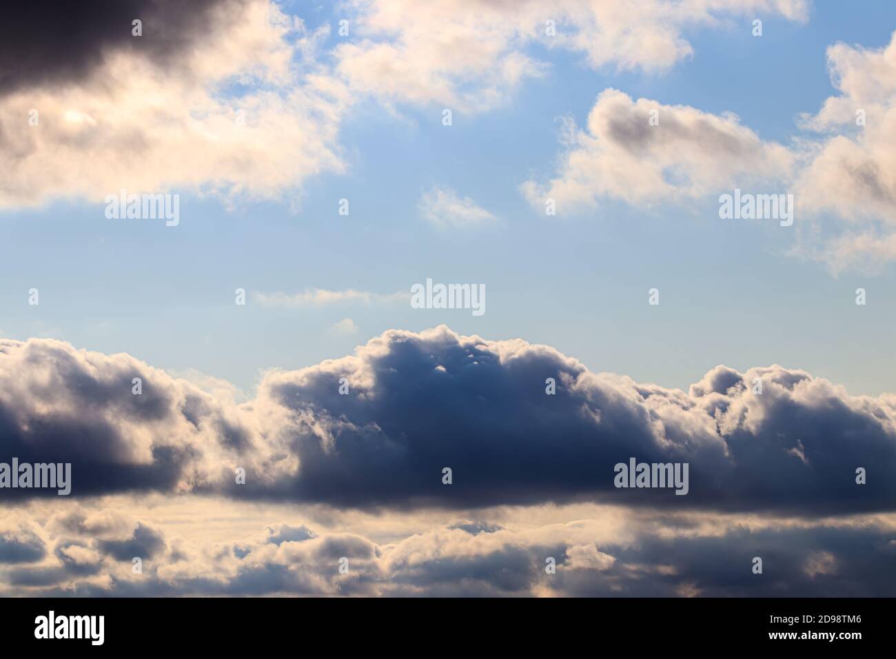 Bright blue sky with dramatic cumulus clouds lit by the daytime sun ...