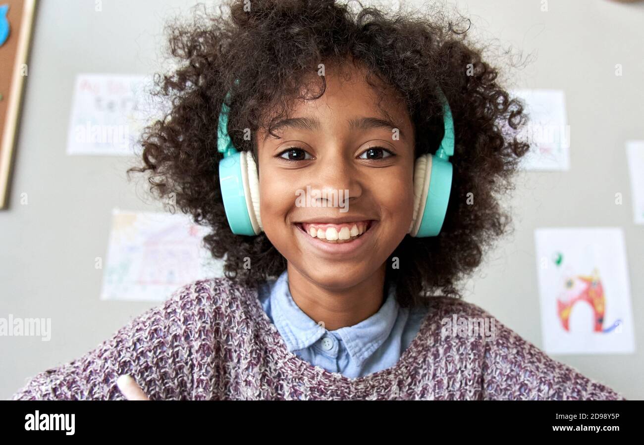 Happy african kid girl wearing headphones looking at camera, headshot. Stock Photo