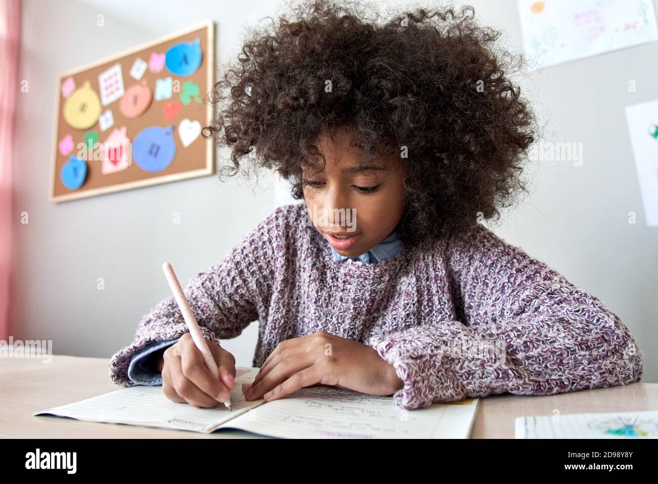 Happy african school child girl studying writing homework, learning at home. Stock Photo