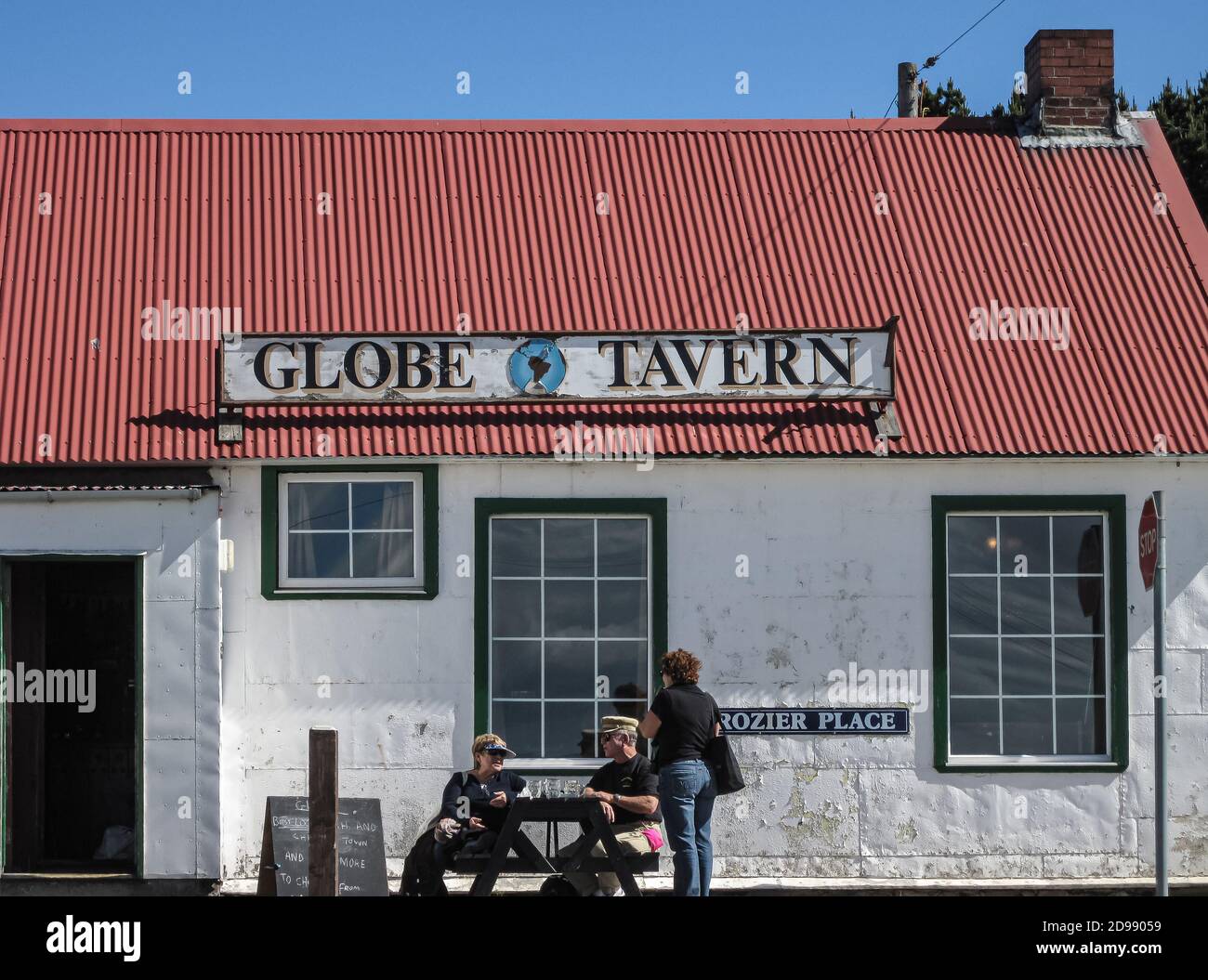 Stanley, Falkland Islands, UK - December 15, 2008: Closeup of entrance to Globe Tavern as white building with red roof under full blue sky with people Stock Photo