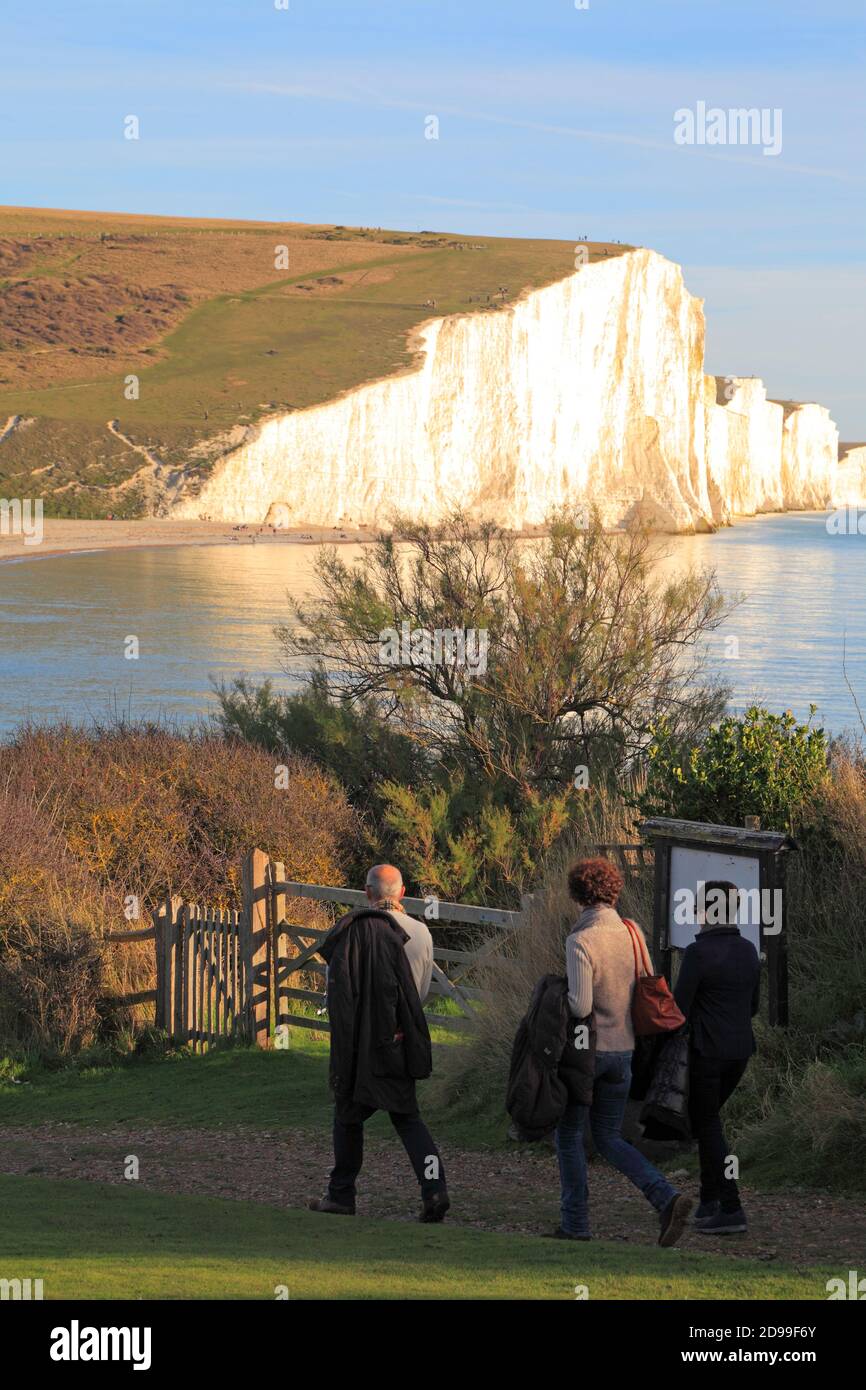 Three people enjoying a winter walk at Seaford Head, with a view of the Seven Sisters white chalk cliffs, East Sussex, UK Stock Photo