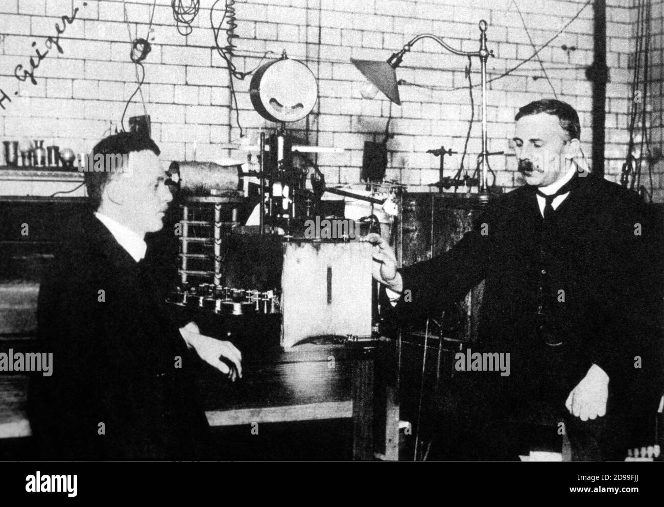 1912 , Cambridge , England : the german  inventor of '  Counter Geiger ' ( 1913 )  HANS GEIGER  ( Neustadt , Germany 1882 - Berlin 1945 ) with ( at right in the photo ) the british physicist Lord ERNEST RUTHEFORD of NELSON  ( Nelson , New Zealand 1871 - Cambridge 1937 ) , discoverer of the ATOMIC MODEL ( 1911 ) with electrons around a nucleus - ATOMIC - ATOMICO - NUCLEO - ELETTRONI - RADIOATTIVITA' - RADIOACTIVITY - FISICA - FISICO - PHYSICS - GENIO -----  Archivio GBB Stock Photo