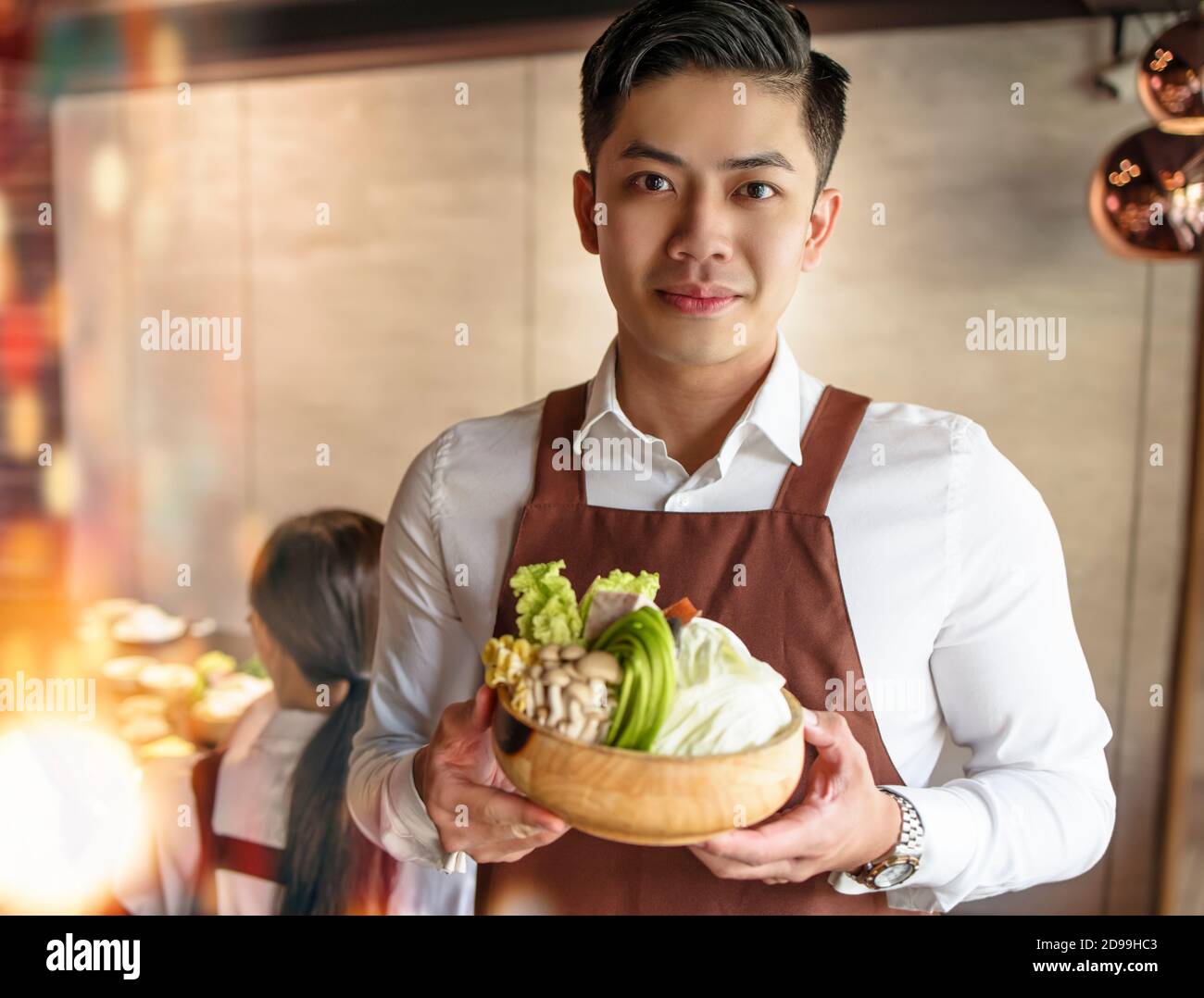 young waiter bring vegetables for hot pot and serving customer  in restaurant Stock Photo