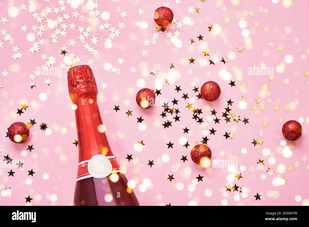 Red Champagne bottle with red Christmas decoration on pink background. Holiday background. Top view, copy space Stock Photo