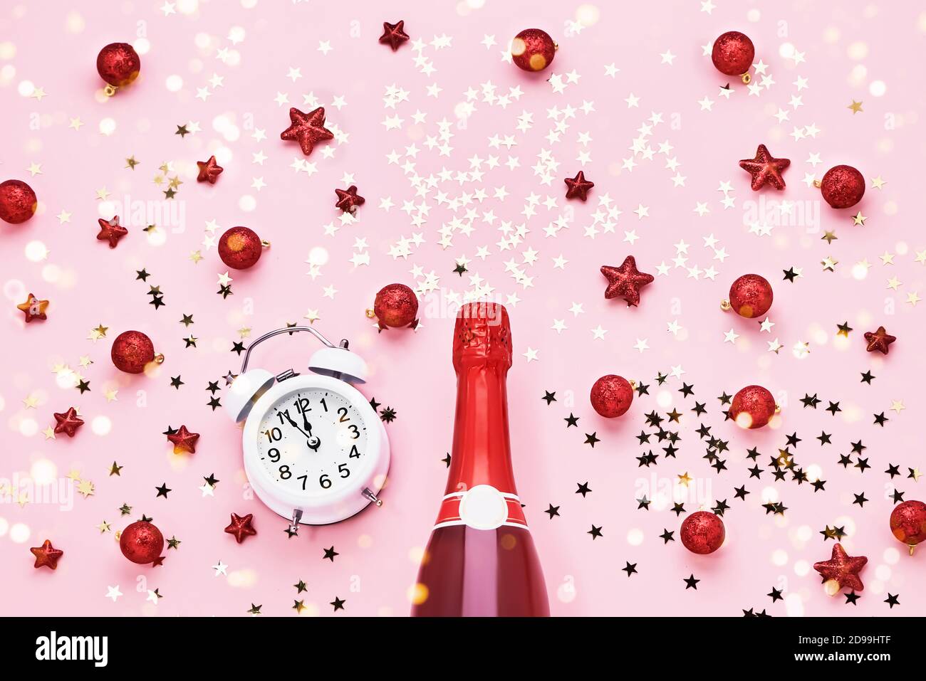 Flat lay of Christmas Celebration. Champagne bottle and alarm clock with Christmas decoration on a pink background. Top view. New Year celebration. Stock Photo